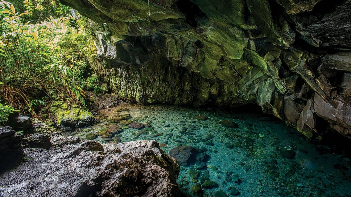 blue freshwater in a cave with green forrest at opening